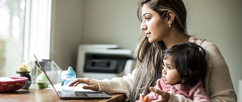 Woman holding a baby while typing on a laptop computer